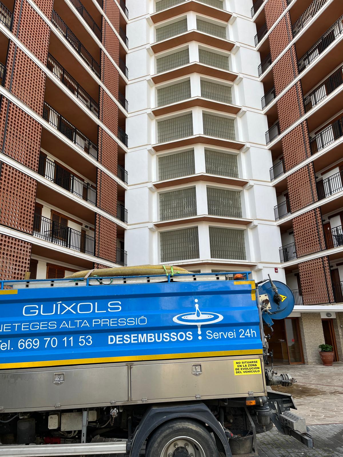 Camión cuba realizando servicios de desatasco y mantenimiento frente a un edificio de varias plantas.