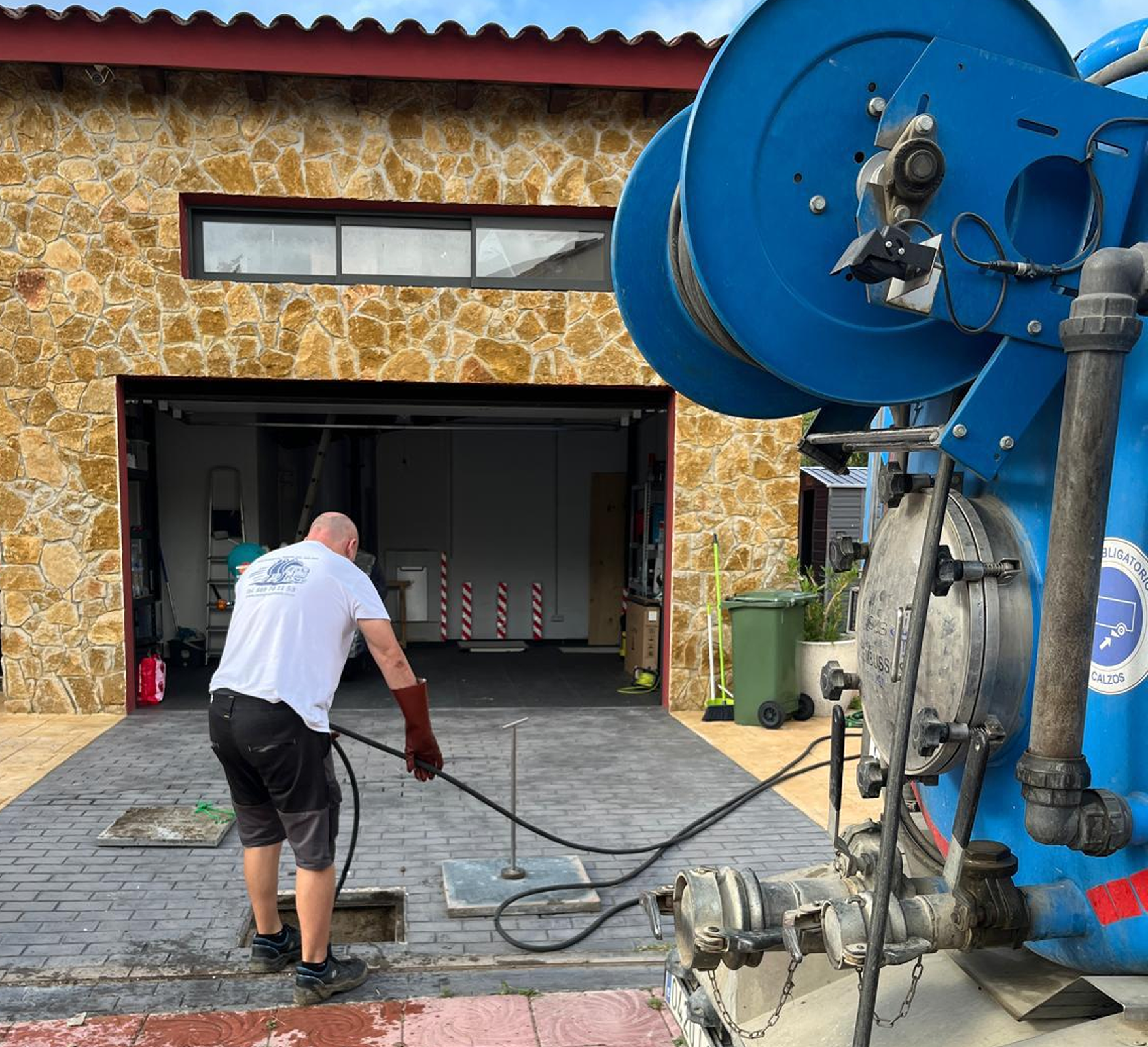 Operario realizando limpieza y desatasco de tuberías con camión cuba en un garaje residencial.